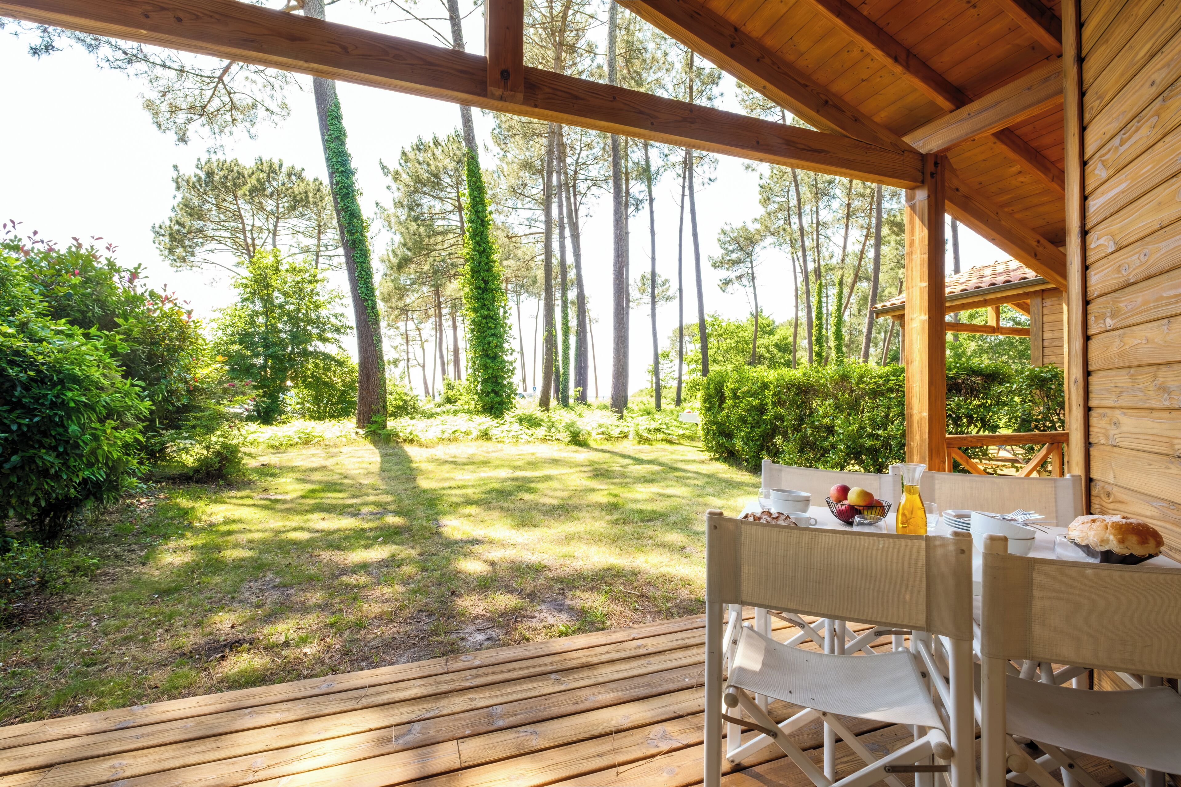A wooden deck with a table set for dining, overlooking a forested area.