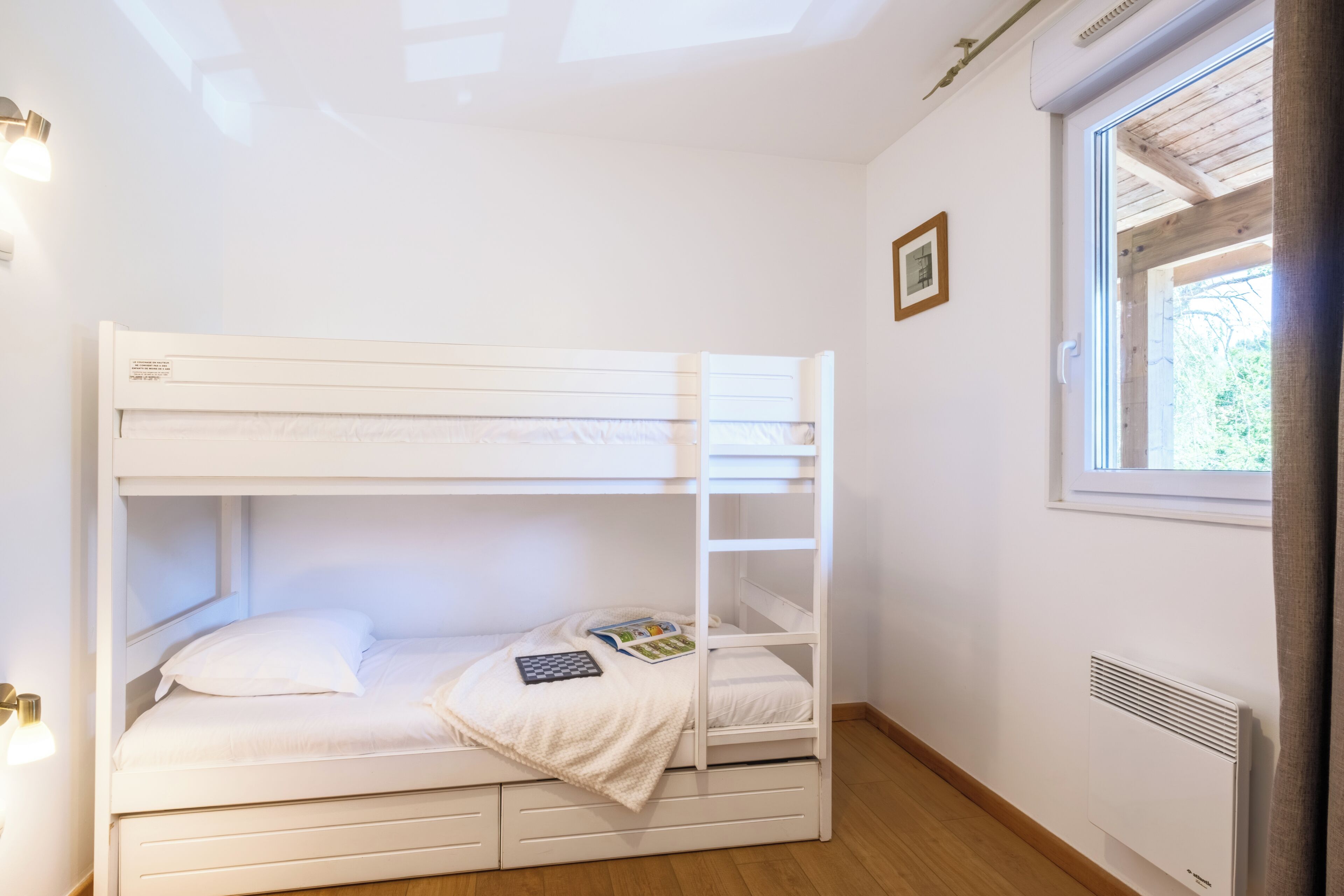 Una cama litera con una cama inferior, una mesita de noche y una ventana que da a zonas verdes.