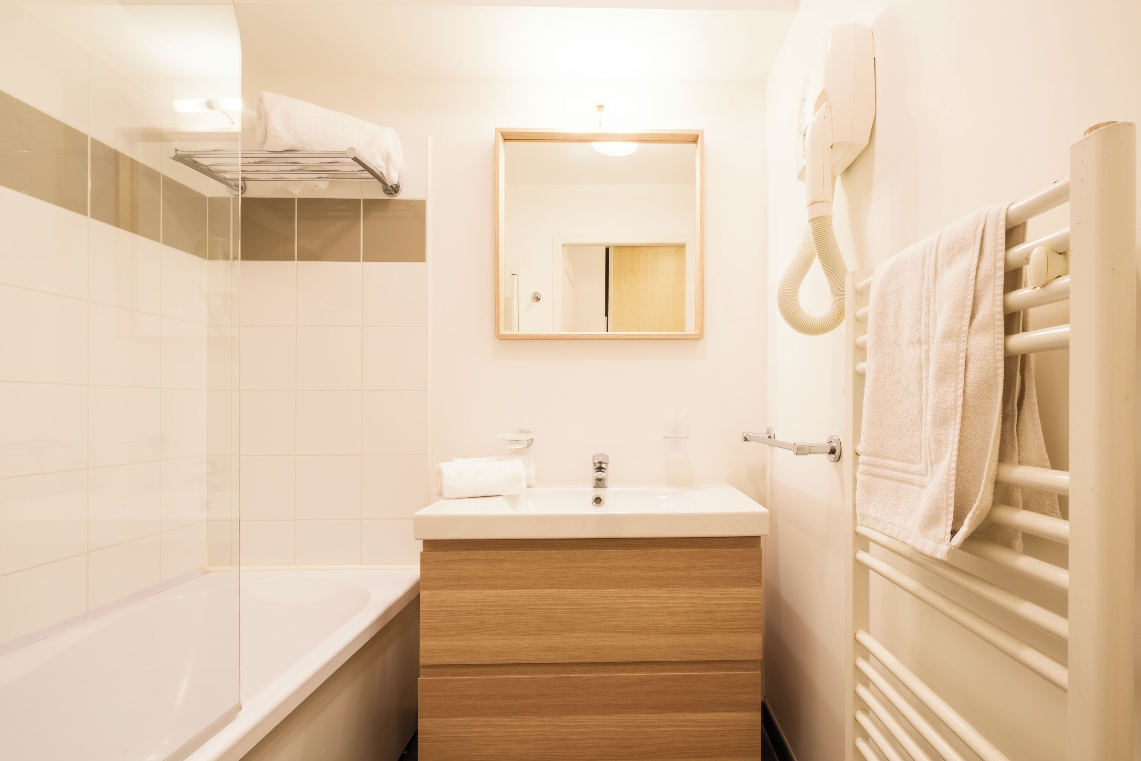Une salle de bain moderne avec une baignoire, un meuble-lavabo en bois, un miroir et un porte-serviettes.