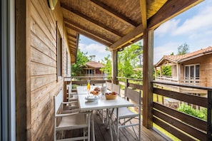 A wooden deck with a table set for dining, overlooking a residential area with houses. - Résidence Pierre & Vacances Les Cottages du Lac (Parentis-en-Born)