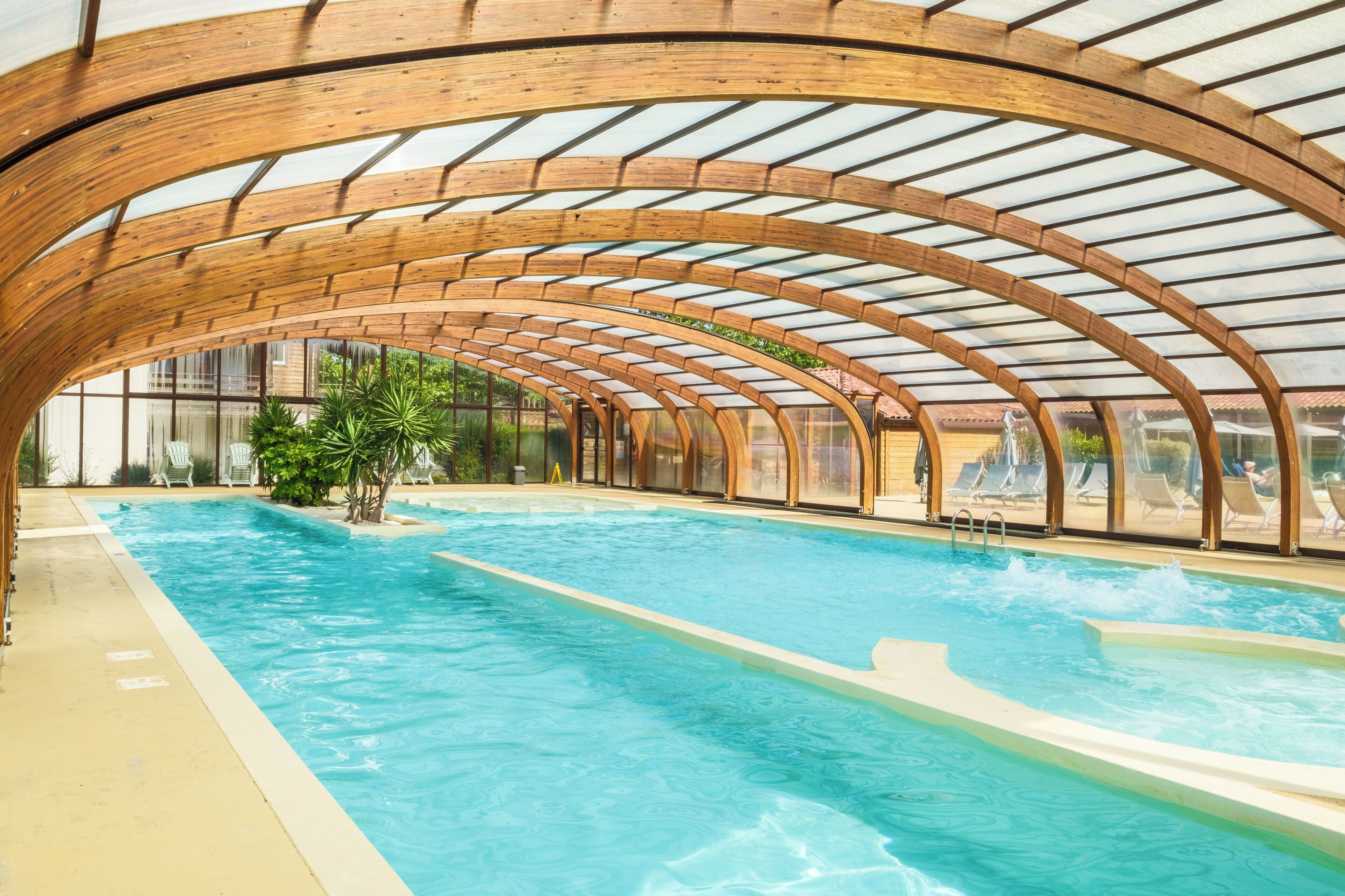 Una piscina interior con techo de madera en arco y paneles de vidrio transparente.