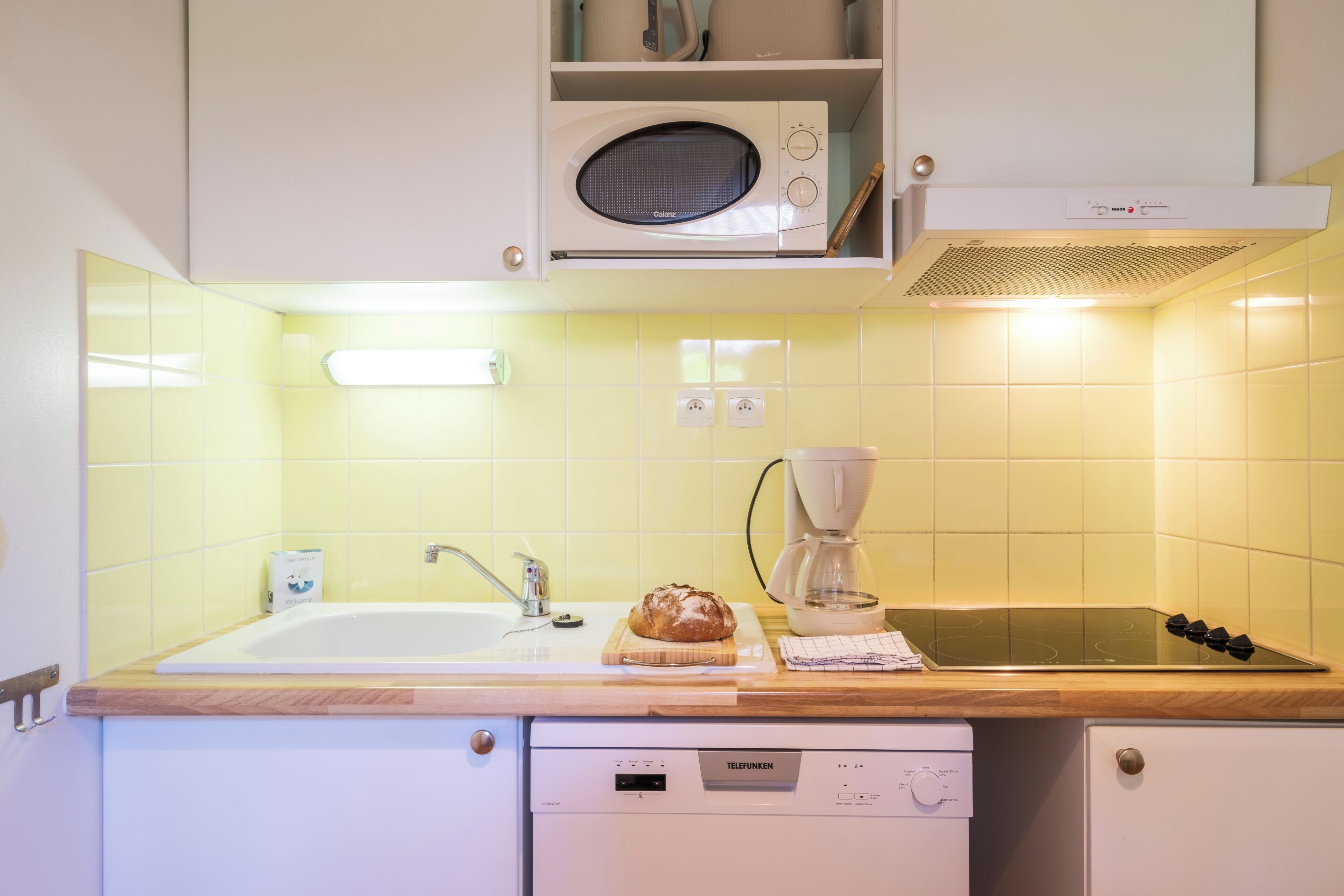 A kitchen with a microwave, coffee maker, and a loaf of bread on the counter.