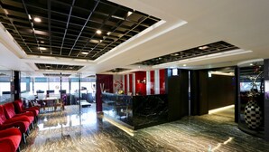 Eine Hotelhalle mit Marmorboden, einer roten Sitzgruppe, einem Empfangsbereich und einem modernen Deckenstil.