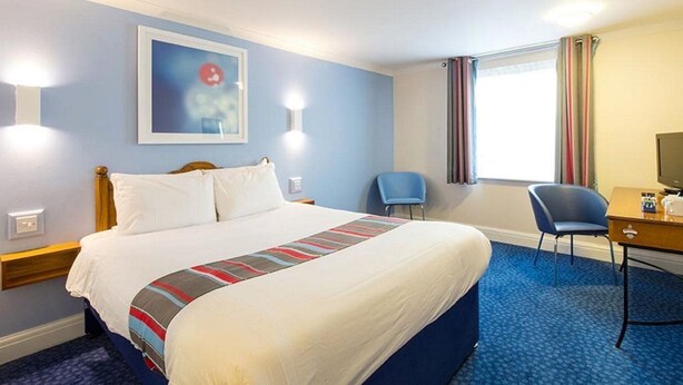 A hotel room with a large bed, a desk with a chair, a television, and a window with curtains. - Travelodge Derby Chaddesden (Derby)