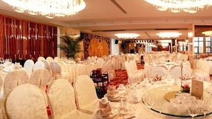 Un salón de banquetes con mesas redondas, sillas blancas y candelabros.