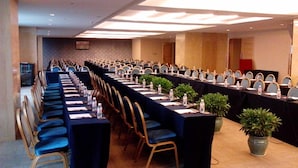 Un salón de conferencias con mesas y sillas dispuestas en filas, equipado con tarjetas de identificación, botellas de agua y micrófonos.