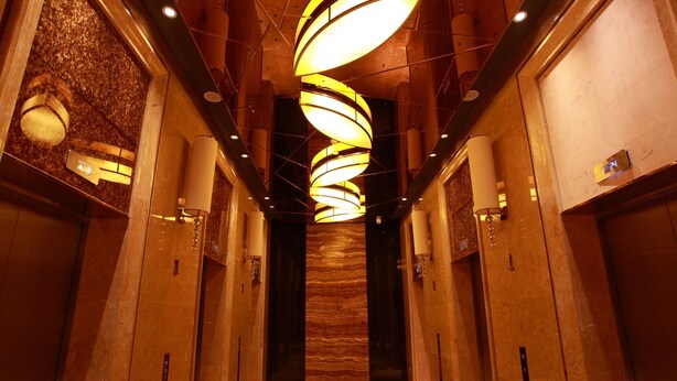 Interior moderno de ascensor con una lámpara en espiral, paredes de mármol y suelo alfombrado.