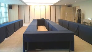 Un salón de conferencias con una larga mesa rectangular, asientos acolchados azules y una paleta de colores neutros.