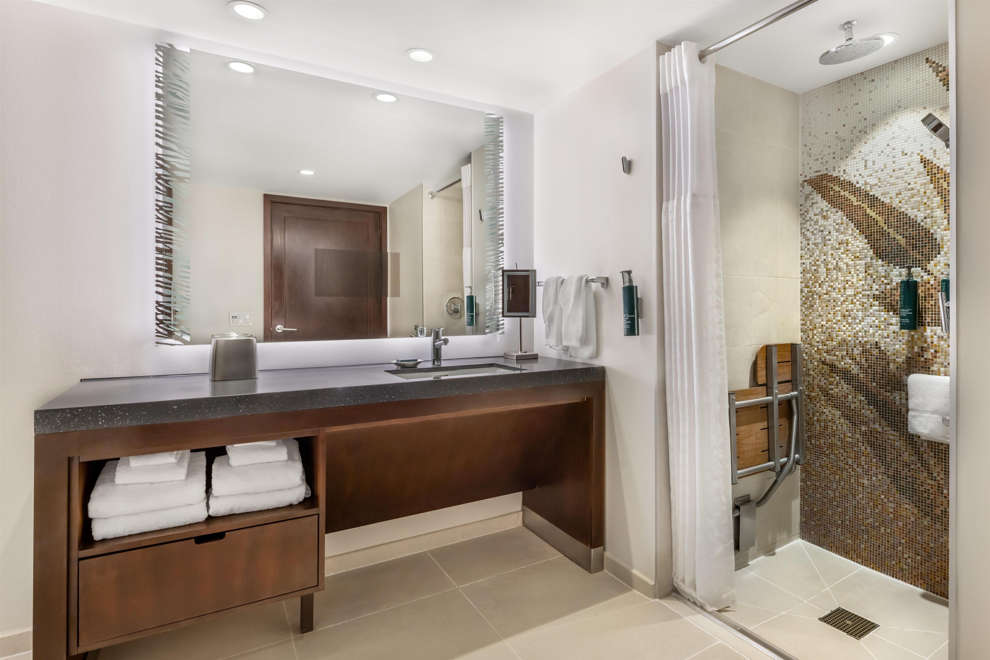 A modern bathroom with a large mirror, a shower with a glass door, and a vanity with a sink and towel storage.