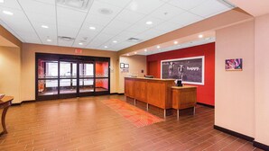 A reception area with a wooden reception desk, a red wall with a 'happy' poster, and an exit sign above the door.