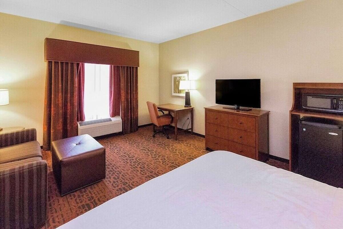 A hotel room with a bed, a desk with a chair, a television, a microwave, and a window with curtains.