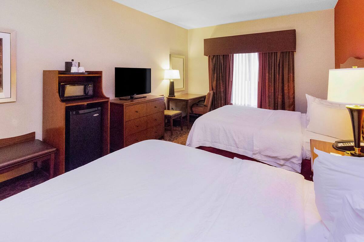 A hotel room with two beds, a desk, a television, a microwave, and a chair.