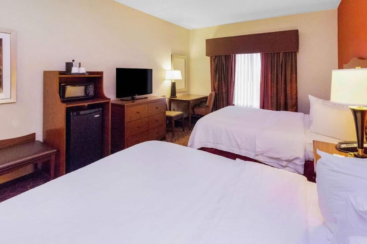A hotel room with two beds, a desk, a television, and a microwave.