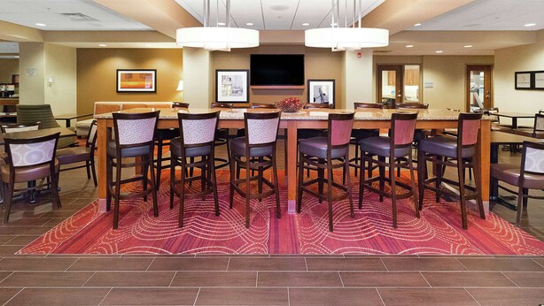 A hotel dining area with a long table, multiple chairs, and a red patterned rug.