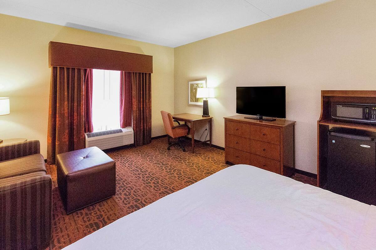 A hotel room with a bed, a desk, a chair, a television, a dresser, and a microwave.