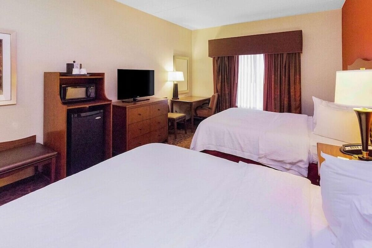 A hotel room with two beds, a desk, a television, a microwave, and a chair.