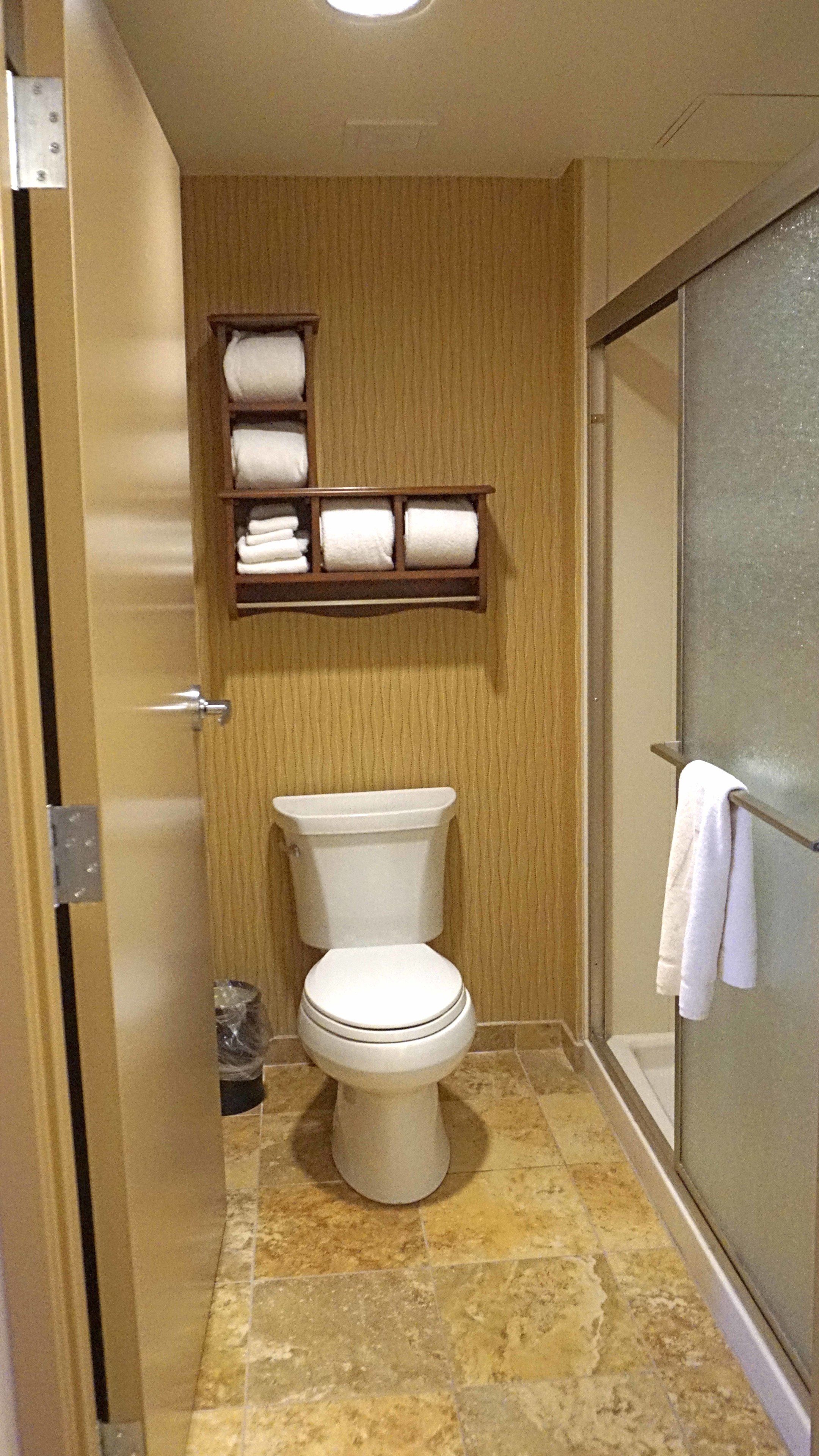A bathroom with a toilet, a towel rack, and a shelf with folded towels.