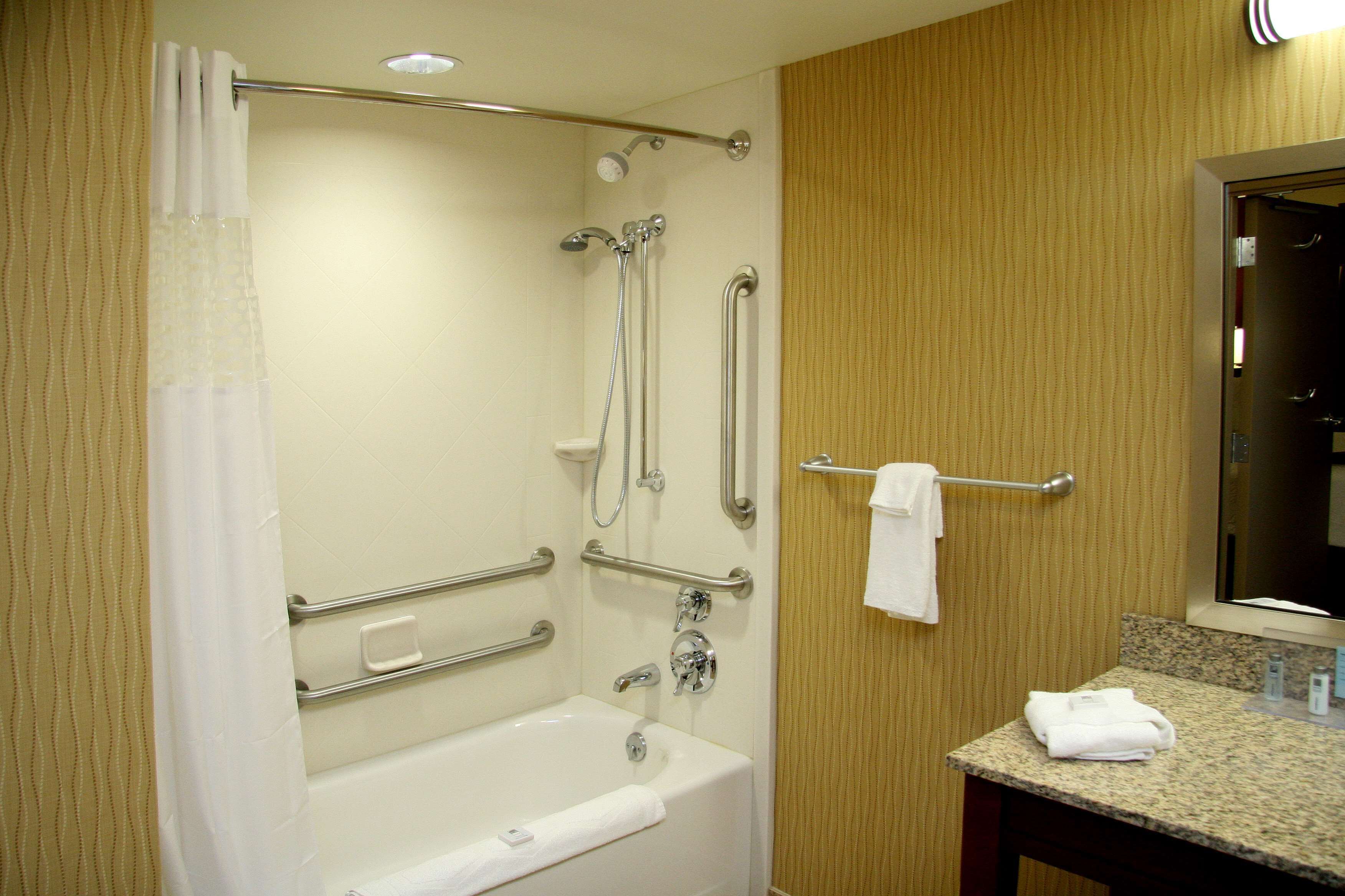 A bathroom with a bathtub, grab bars, a showerhead, and a towel rack.
