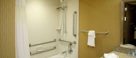 A bathroom with a bathtub, grab bars, a showerhead, and a towel rack.