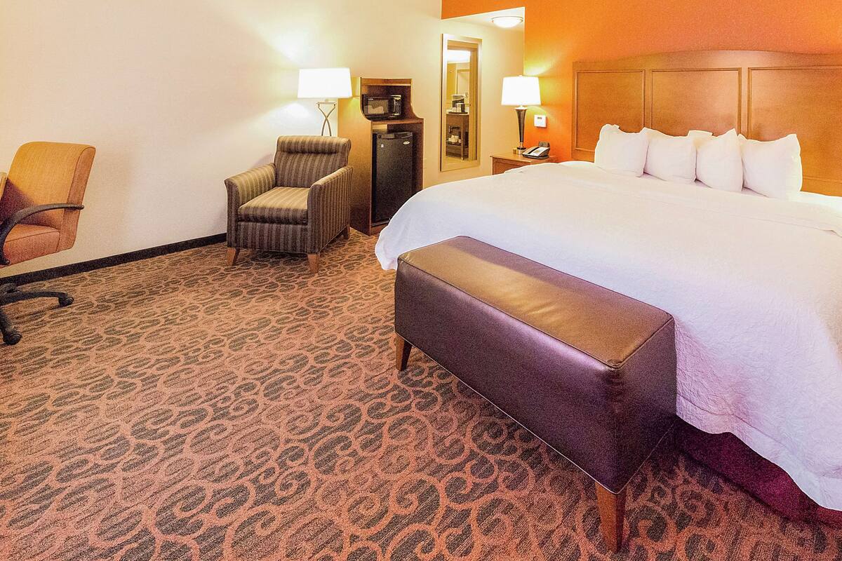 A hotel room with a large bed, a chair, a desk with a computer, and a minibar.