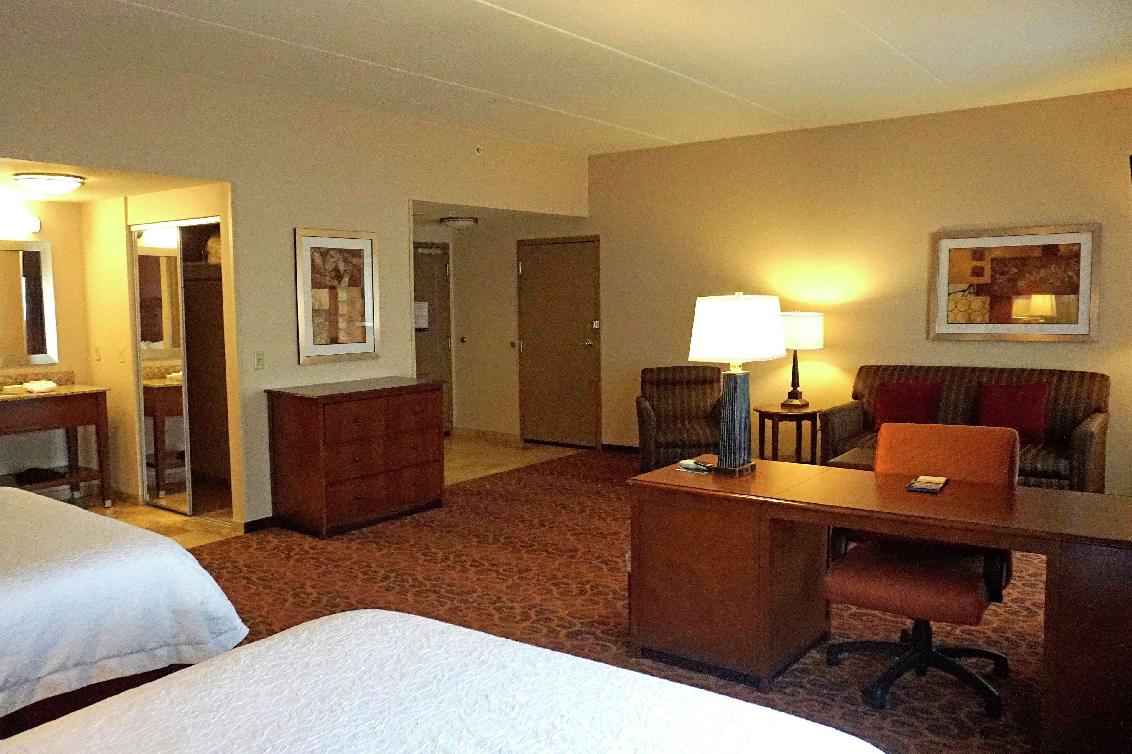 A hotel room with two beds, a desk, a chair, a lamp, and a couch.
