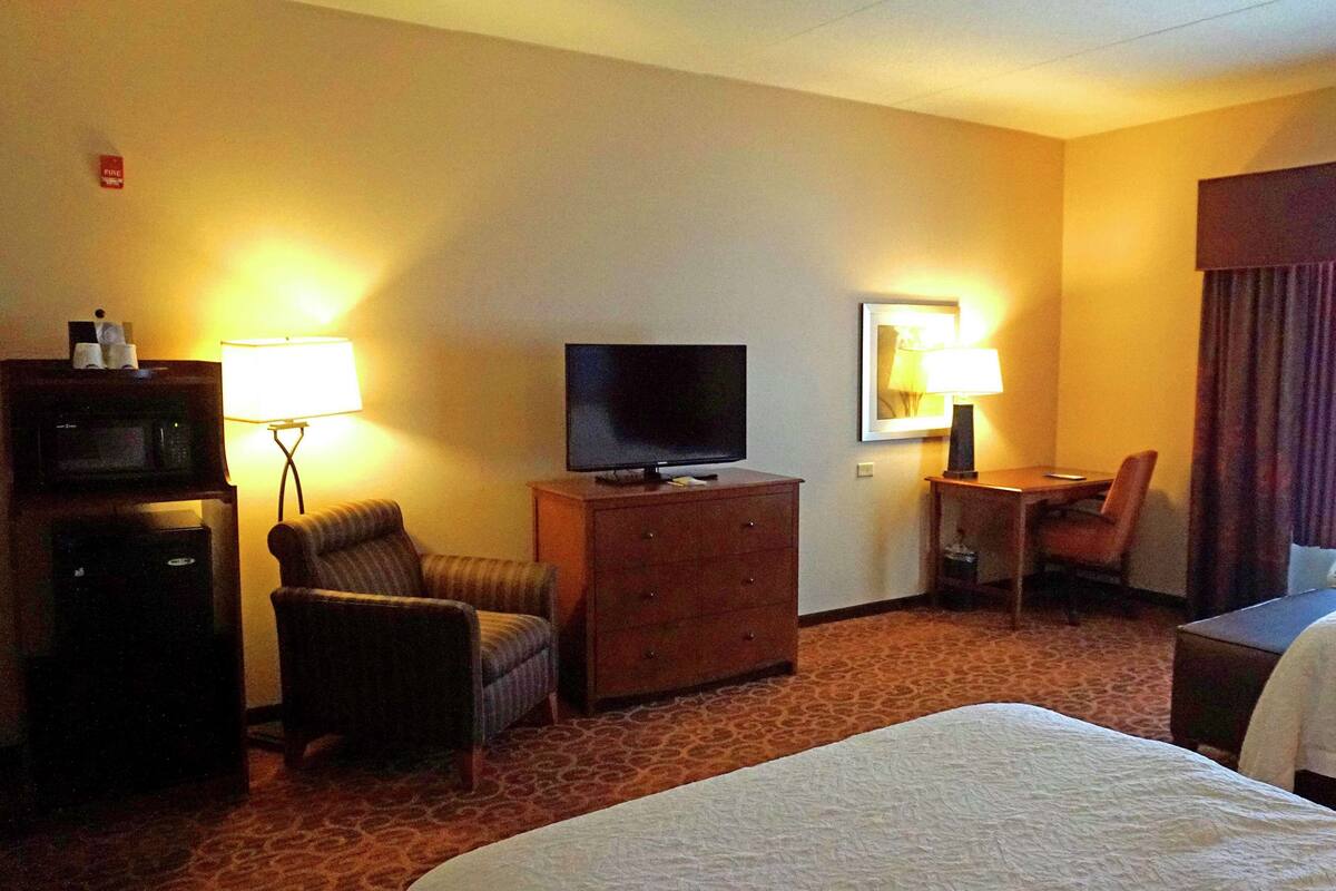 A hotel room with a bed, a television on a wooden dresser, a chair, a desk, and two lamps.