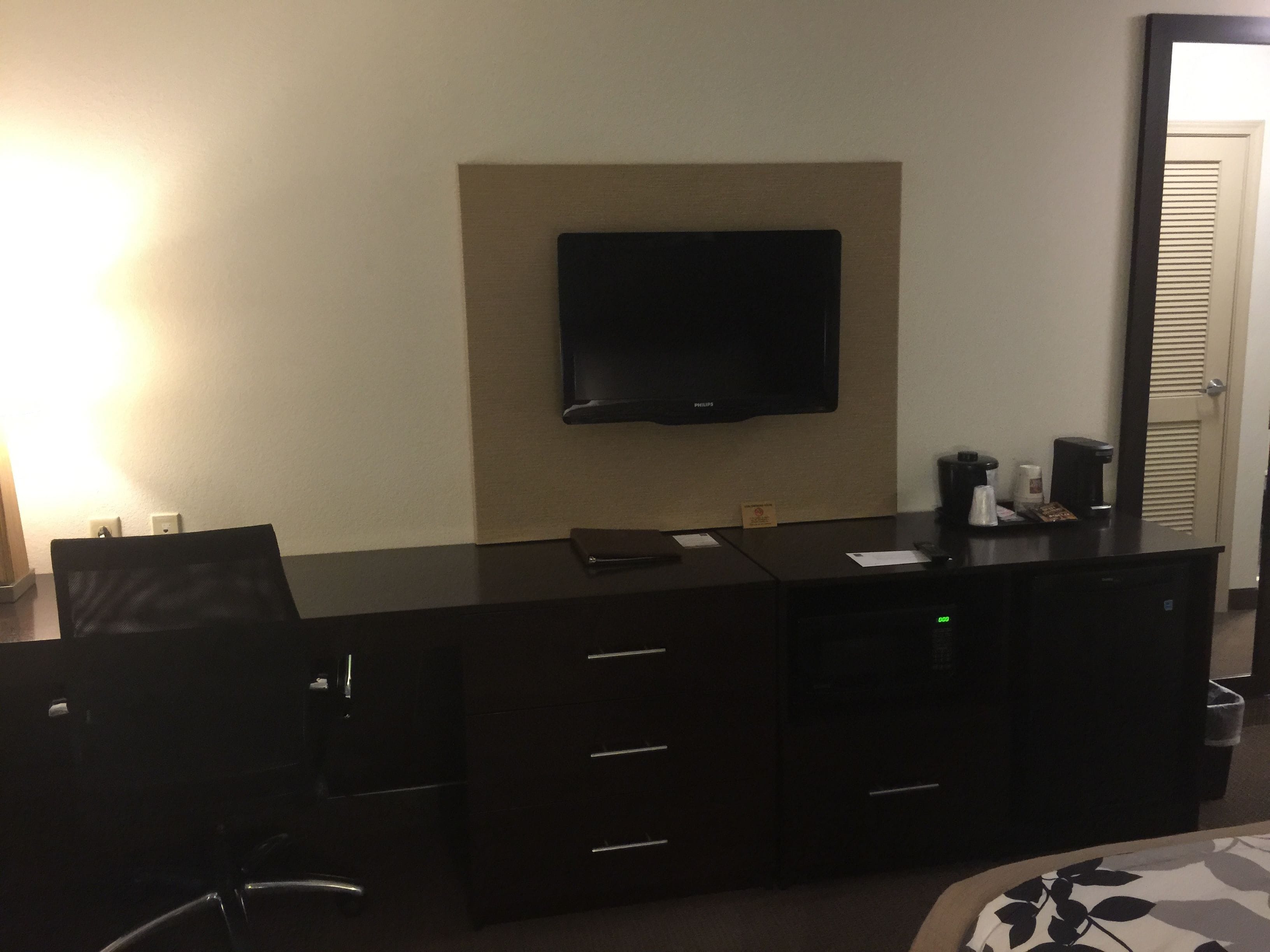Habitación de hotel con televisor de pantalla plana, escritorio con cajones, silla y cafetera.