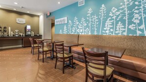 Ein Restaurant mit Holztischen und -stühlen, einer Theke mit Kaffeemaschinen und einer Wand mit einem Baum-Wandbild.