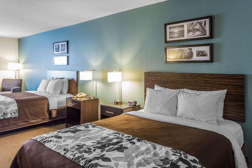 A hotel room with two beds, a desk, a chair, and framed pictures on the wall.