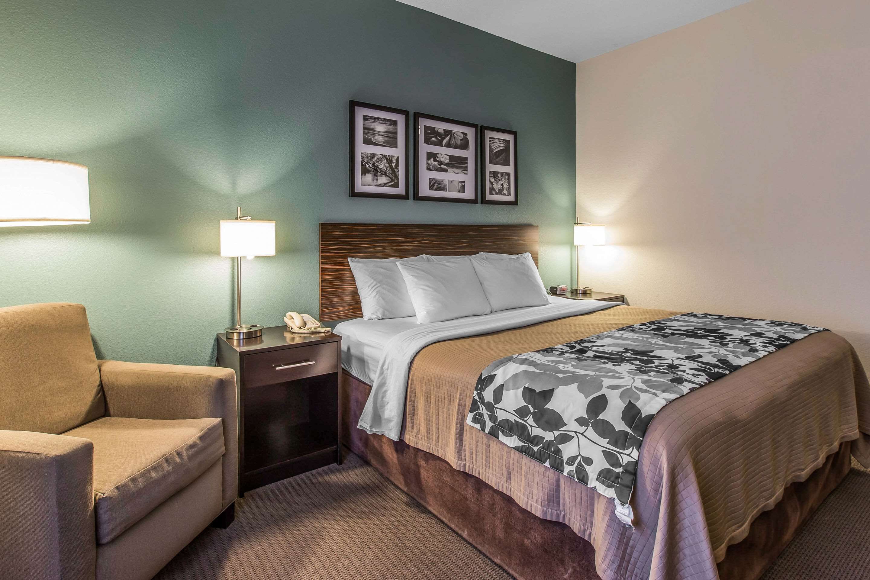 A hotel room with a bed, two bedside lamps, a chair, a nightstand with a phone, and three framed pictures on the wall.