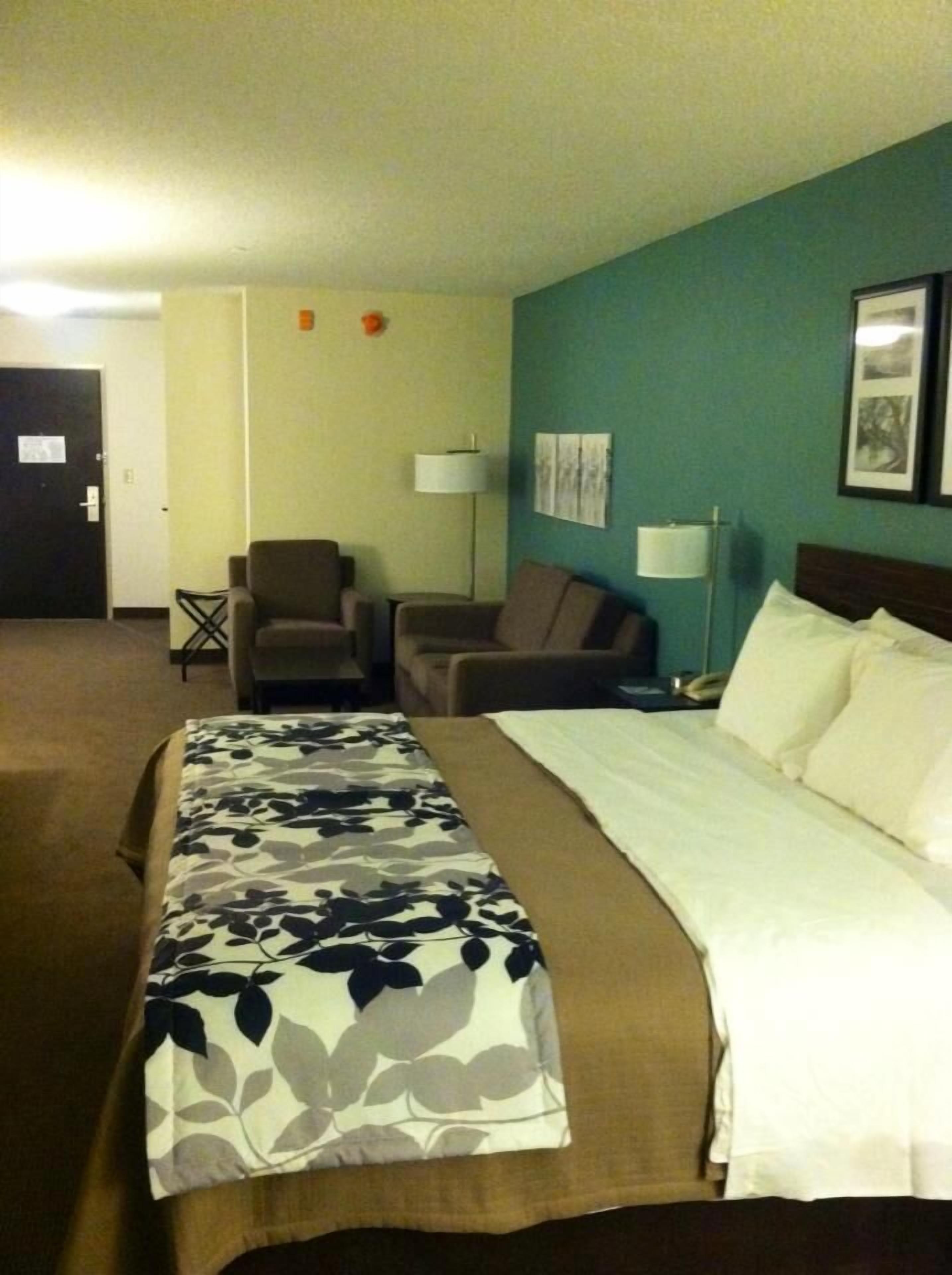 A hotel room with a bed, two armchairs, a small table, and a lamp.