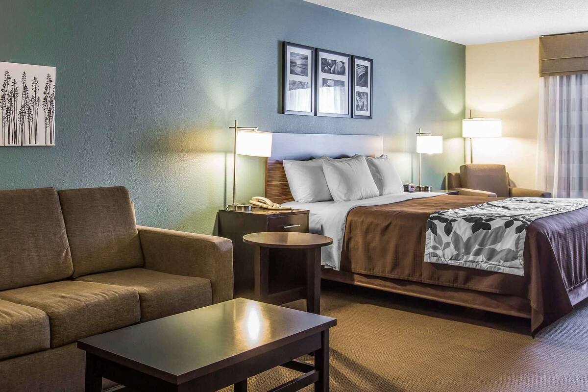 A hotel room with a bed, a sofa, a small table, and two lamps.
