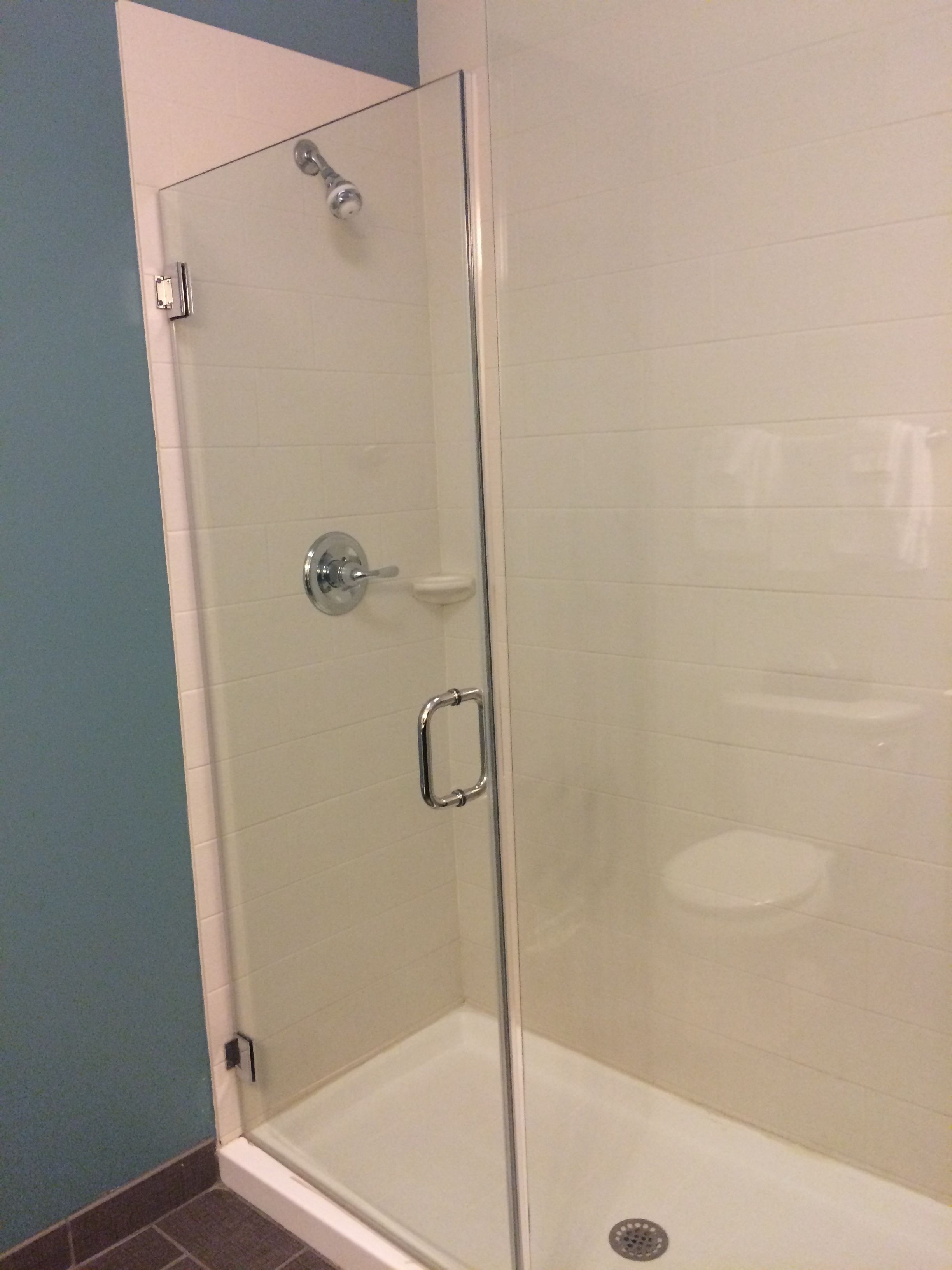 Een douchecabine met glazen wanden, een witte betegelde muur, een chroomdouchekop en een handdouche.