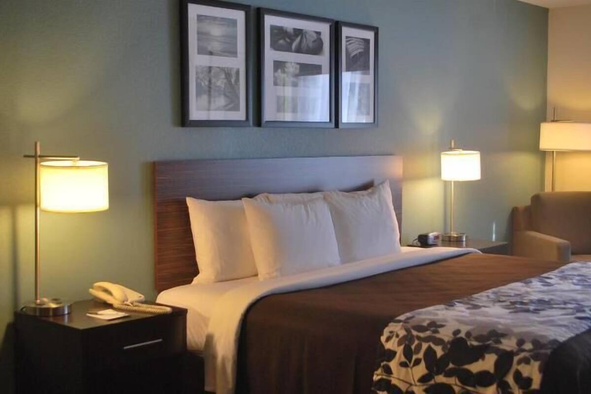 A hotel room with a bed, two bedside lamps, a chair, and three framed pictures on the wall.