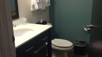 A bathroom with a white sink, dark cabinet, and a toilet. There are towels hanging on the wall and a trash bin on the floor.