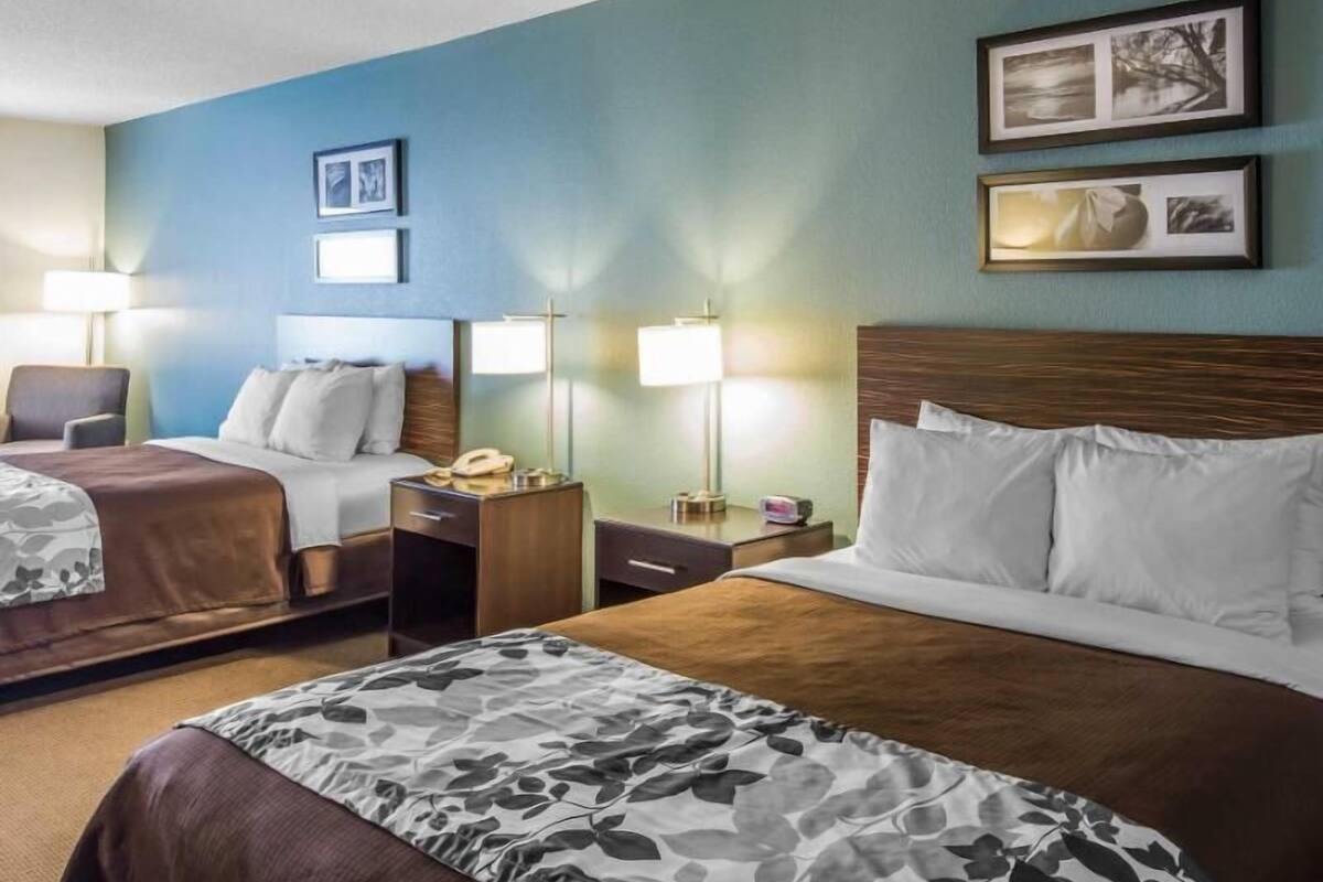 A hotel room with two beds, a desk, a chair, and two bedside lamps.
