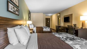 A hotel room with a large bed, a desk with a chair, a television, and framed pictures on the wall.