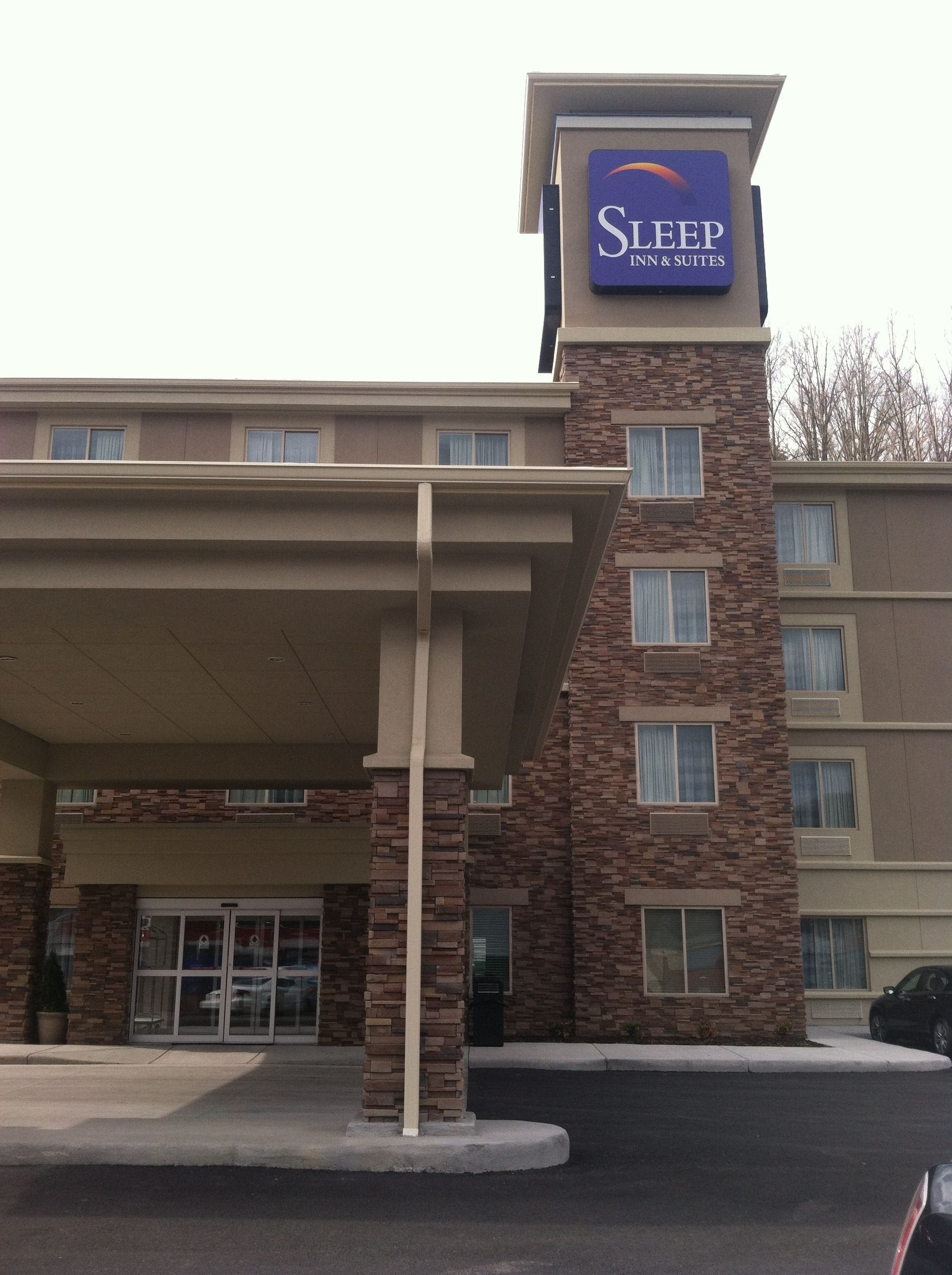 A Sleep Inn & Suites building with a stone facade, a covered entrance, and a signboard.
