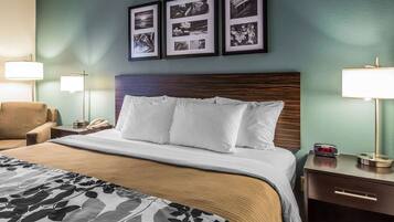 A hotel room with a large bed, a wooden headboard, a nightstand with a lamp, a chair, and framed pictures on the wall.