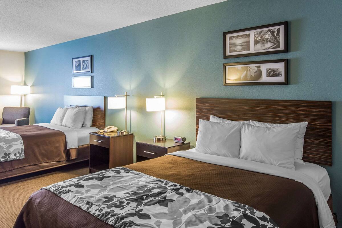 A hotel room with two beds, a desk, a chair, and a nightstand.
