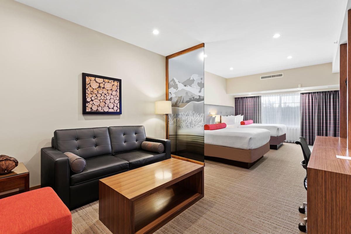 Ein Hotelzimmer mit einer schwarzen Ledersofa, einem Holztisch, einem Bett mit weißem Kopfteil und einem großen Spiegel.