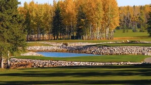 A golf course with a pond, surrounded by trees with autumn foliage.