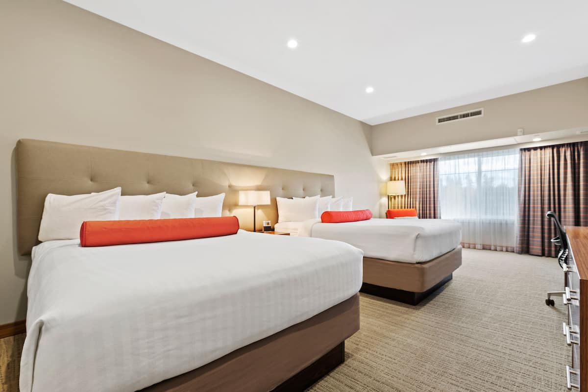 Ein Hotelzimmer mit zwei Betten, einem großen Fenster mit Vorhängen, einem Schreibtisch und einer Lampe.
