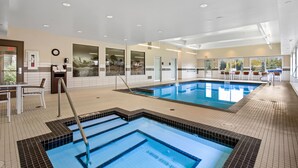 A large indoor swimming pool with clear blue water, surrounded by tiled walls and a wooden deck area.
