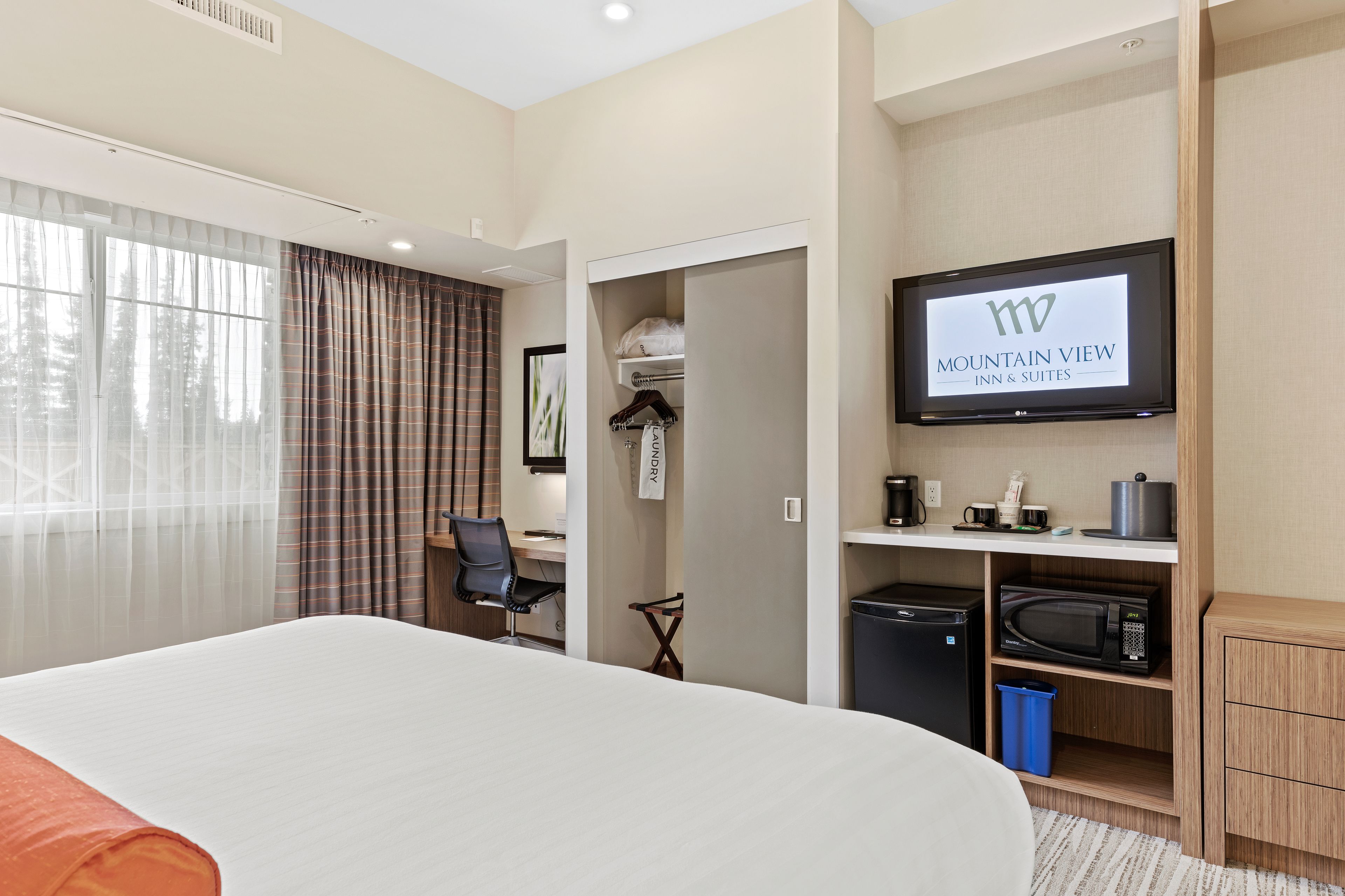 A hotel room with a bed, a desk, a television, a microwave, and a closet.