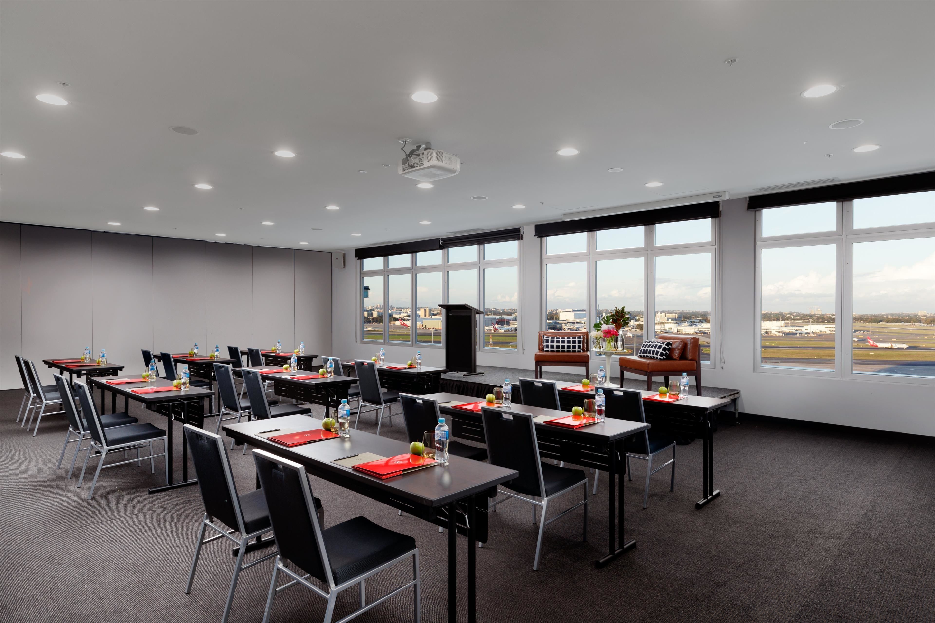 Un salón de conferencias con mesas, sillas y un amplio ventanal con vista al aeropuerto.