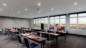 Un salón de conferencias con mesas, sillas y un amplio ventanal con vista al aeropuerto.