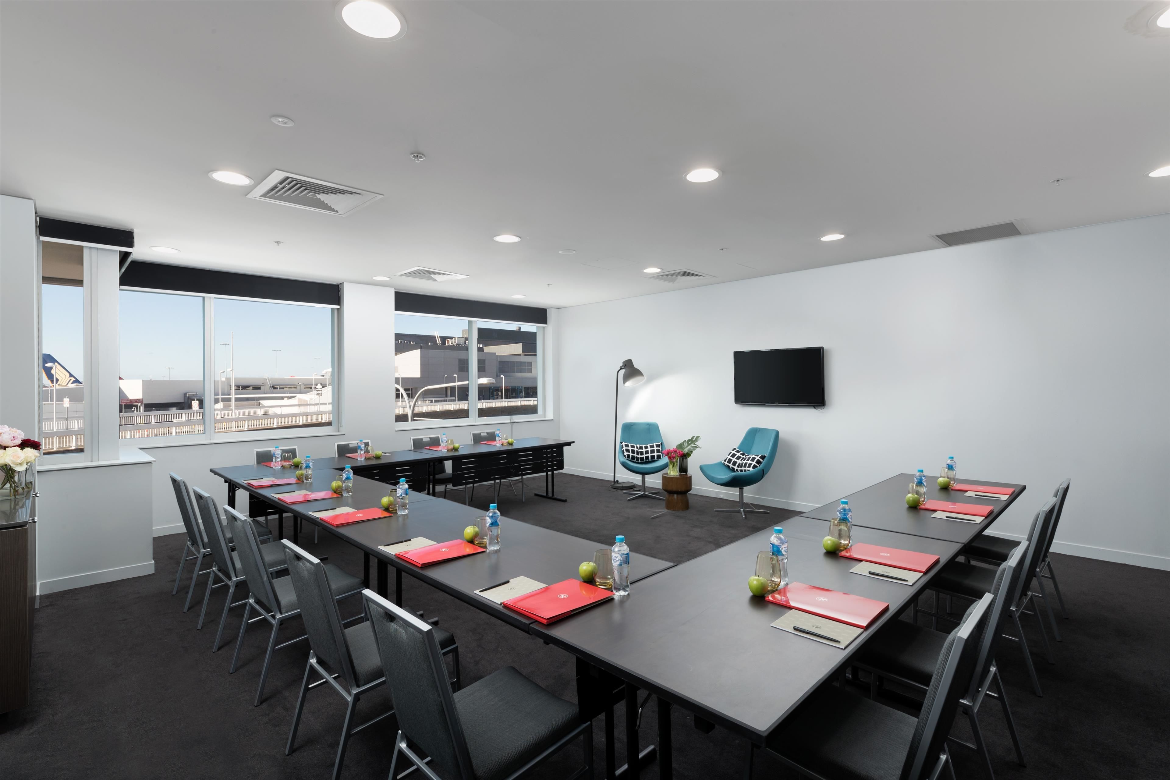 A modern conference room with a long table, black chairs, and a large window offering a city view.