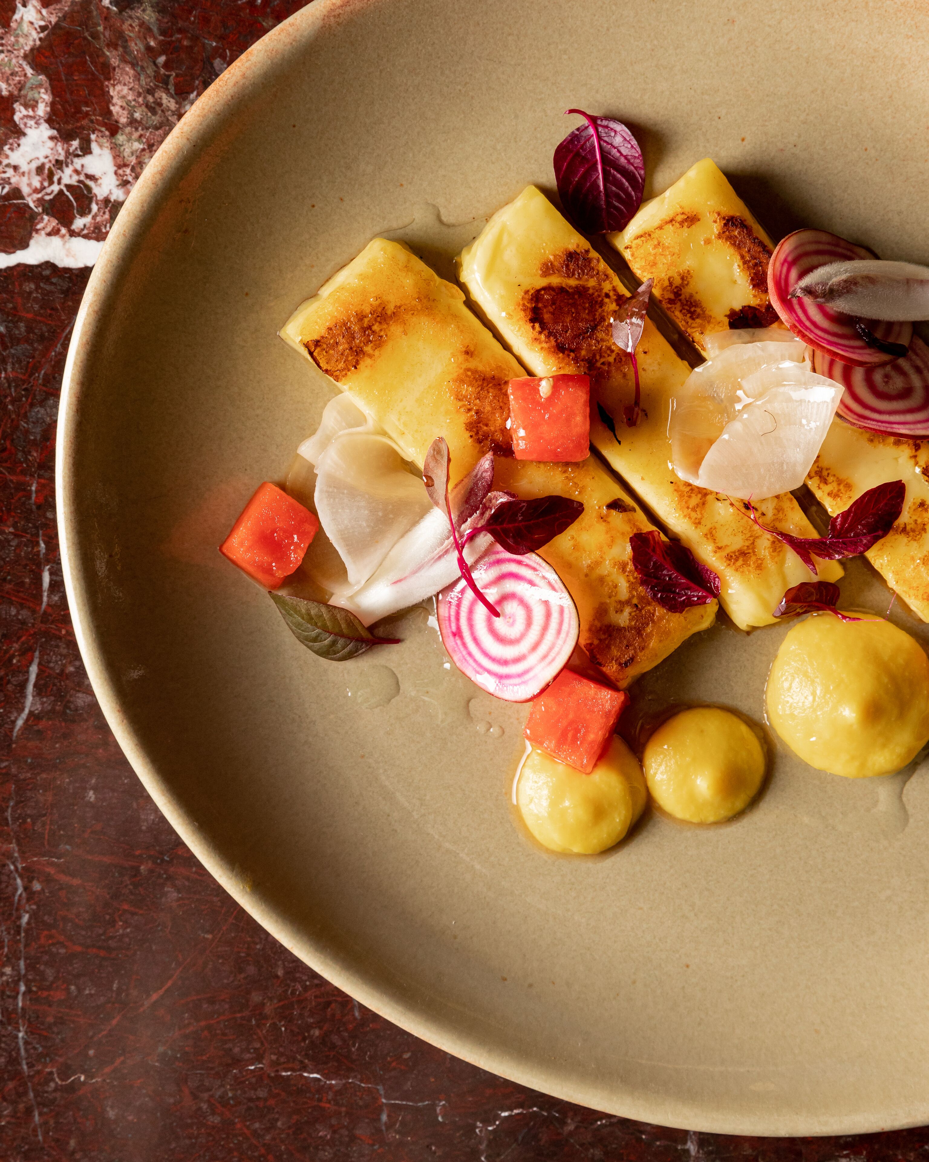 A plate with food items including what appears to be a pastry, slices of beetroot, and a dollop of a yellow sauce.