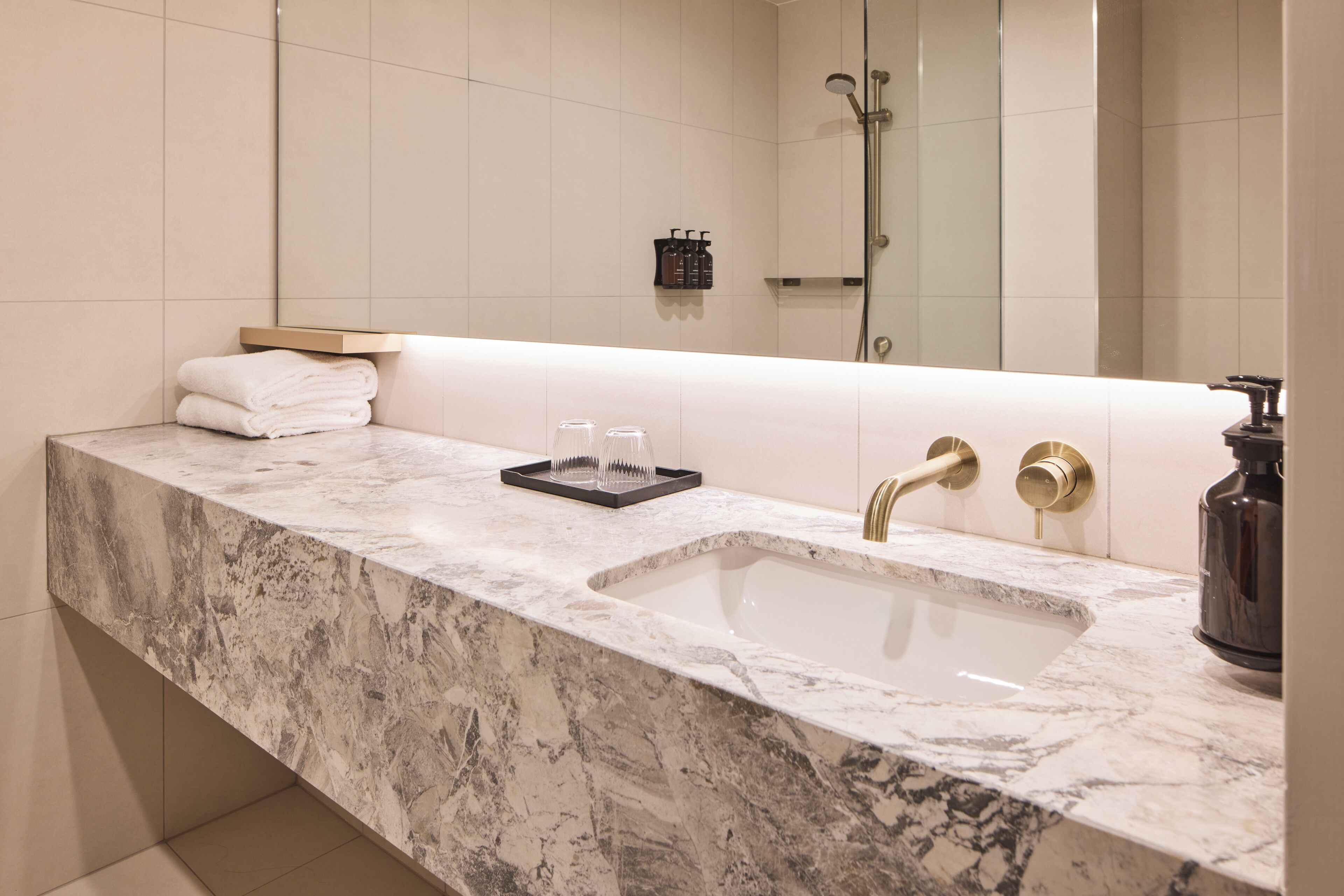 A bathroom with a marble sink, two gold faucets, a glass soap dish, and a towel rack.